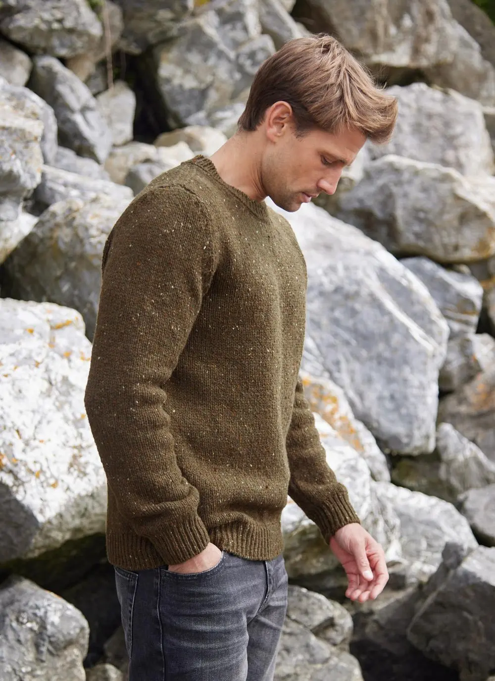 Man on a beach wearing an olive flecked fisherman crew neck sweater