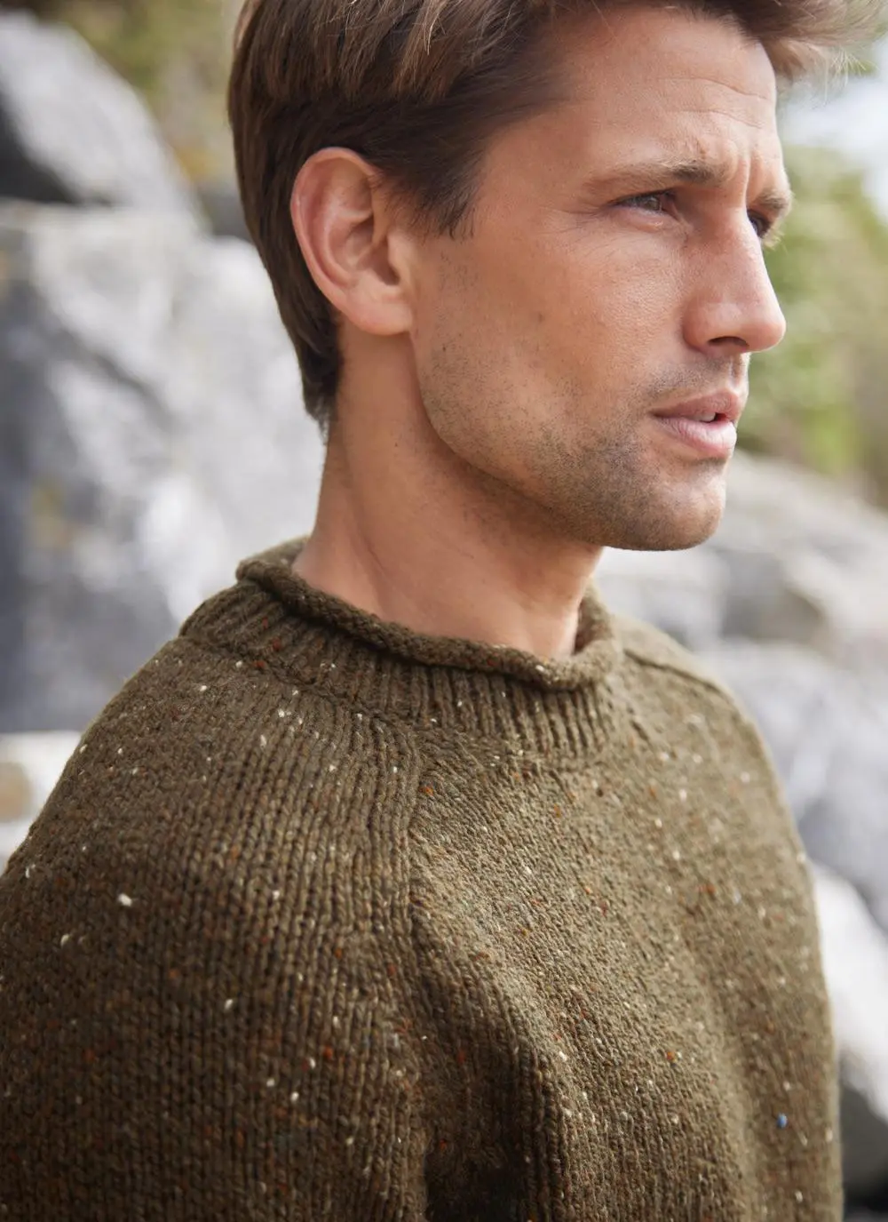 man standing by rocks wearing olive colored knit sweater, close up of neck