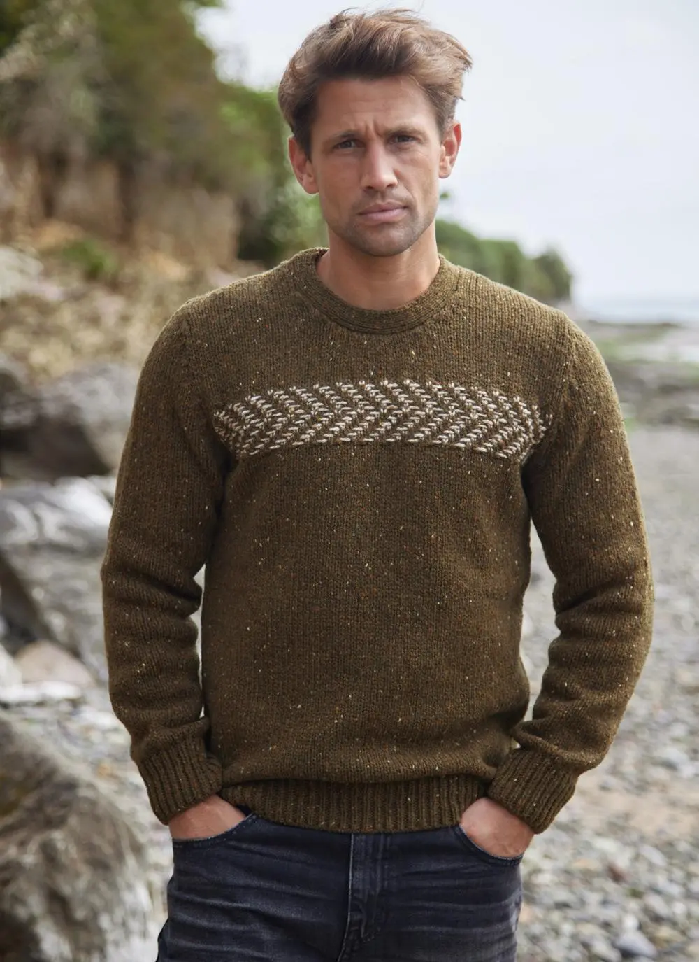 Man on beach wearing two tone crew neck sweater, hands in pockets