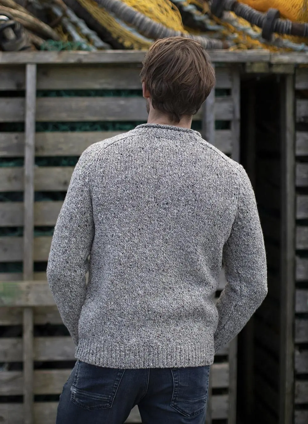 back angle shot of man standing against grey wooden fence wearing grey sweater