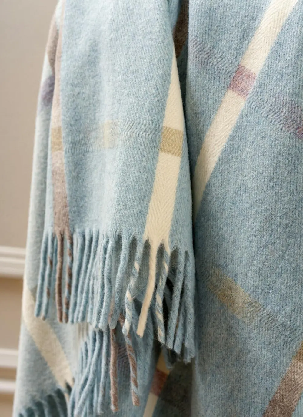 Close-up of light blue check lambswool fringed throw draped across wooden chair