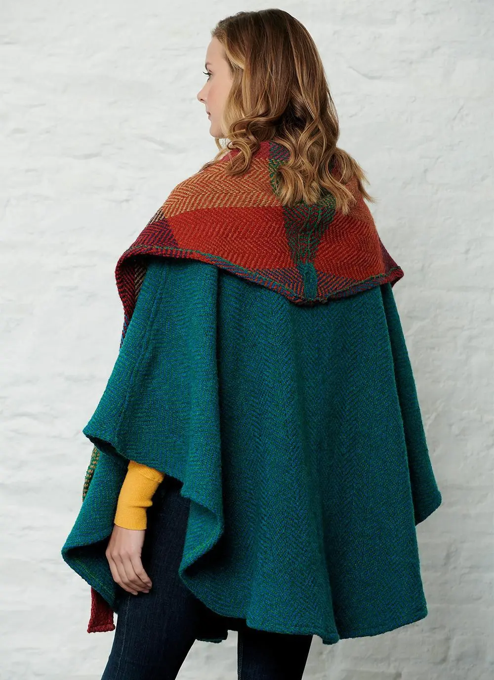 Back angle studio shot of women wearing green cape with detachable multi-colored hood.