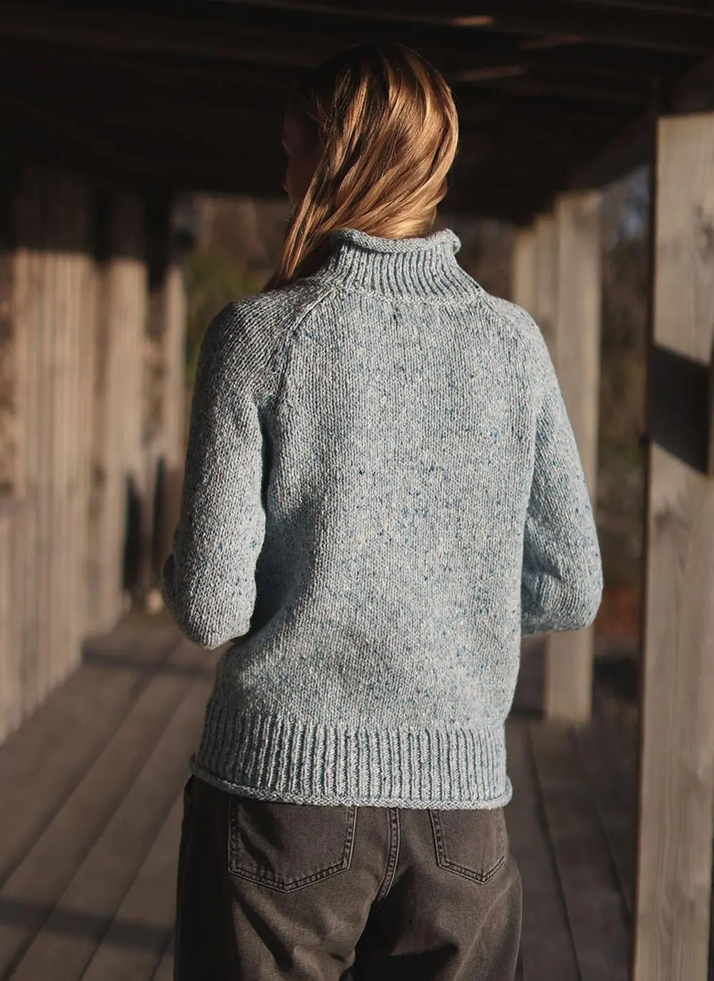 back angle shot of blonde woman wearing blue sweater with stable in background