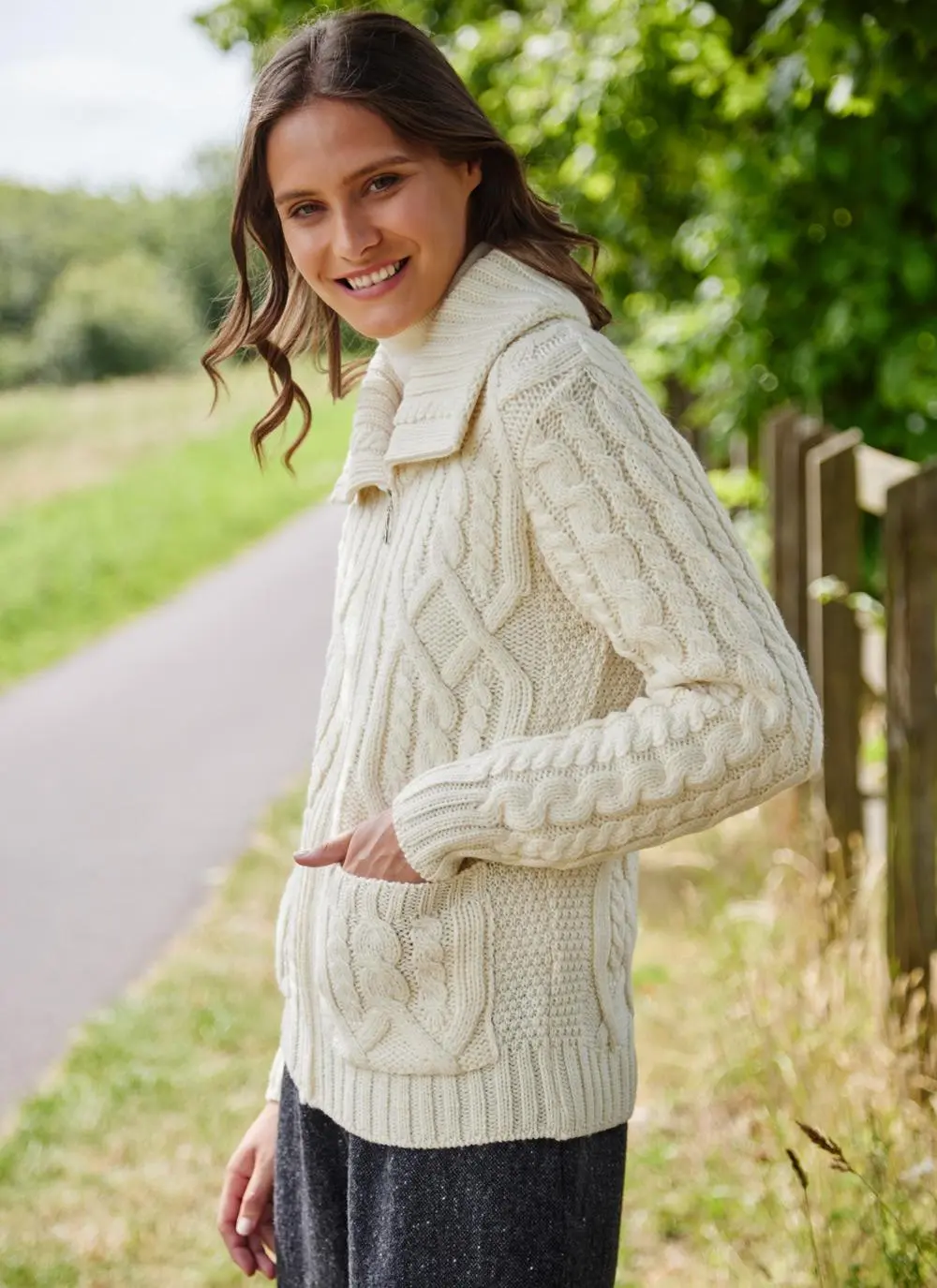 brown haired woman in park wearing cream aran zip cardigan with hand in pocket