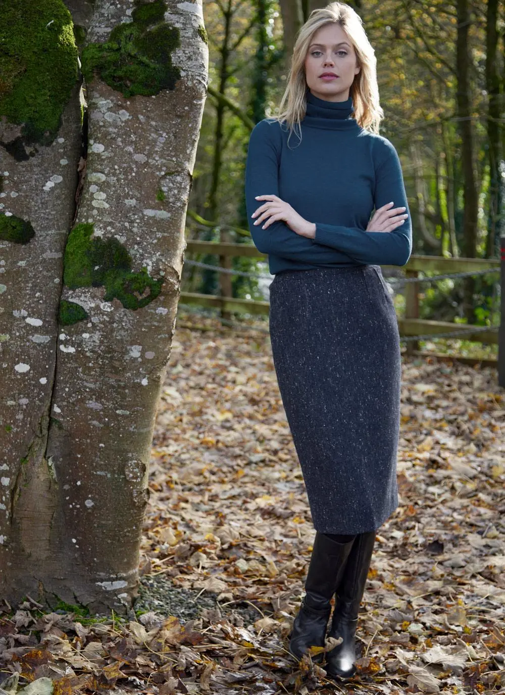 Woman standing in forest wearing denim tweed straight skirt, arms folded