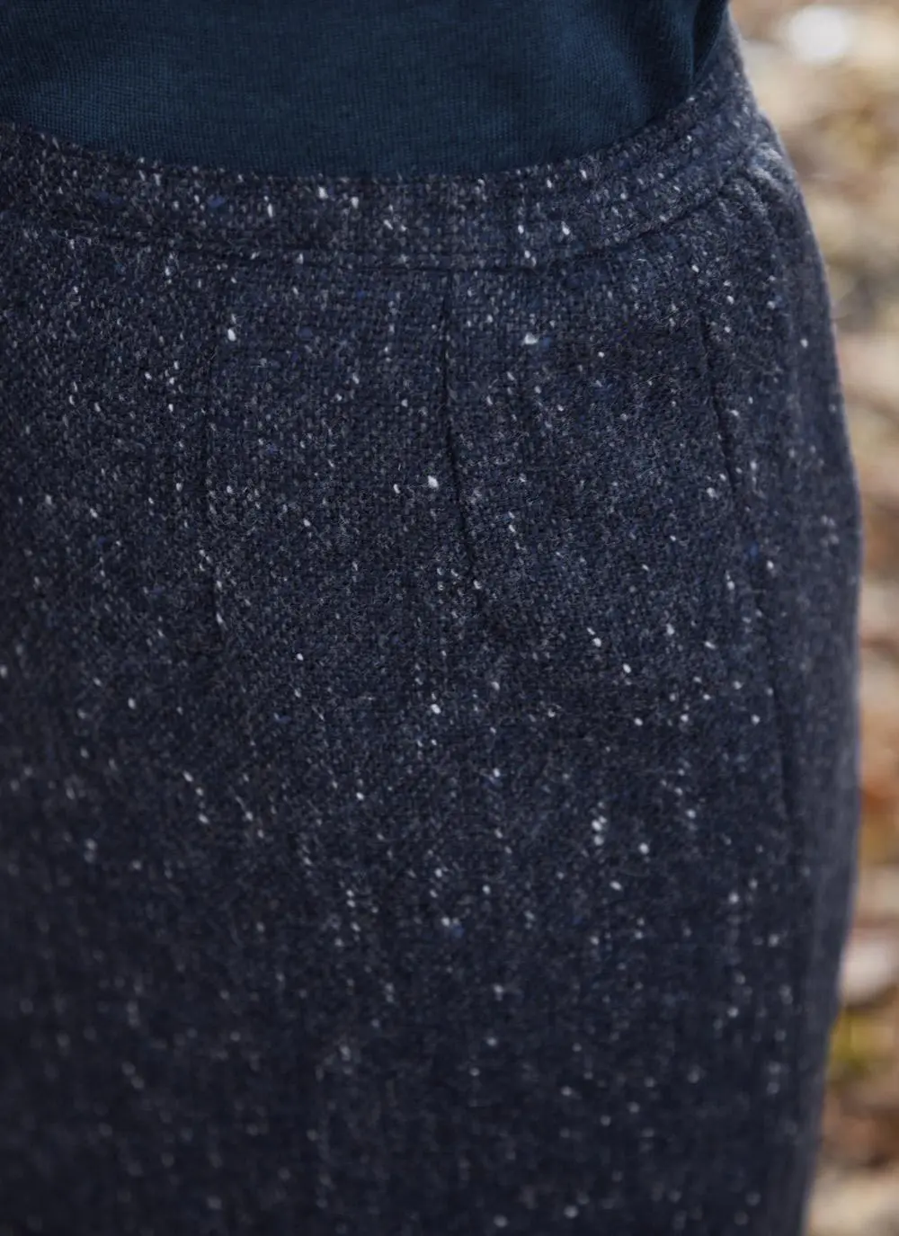 Woman standing in forest wearing denim tweed straight skirt, close up