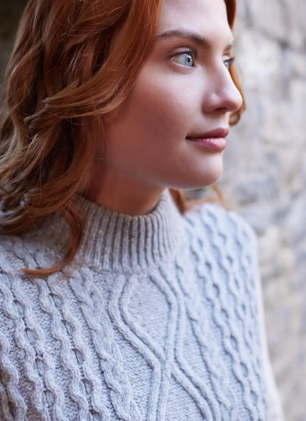 close-up of red haired woman standing in stone abbey wearing a grey sleeveless aran sweater