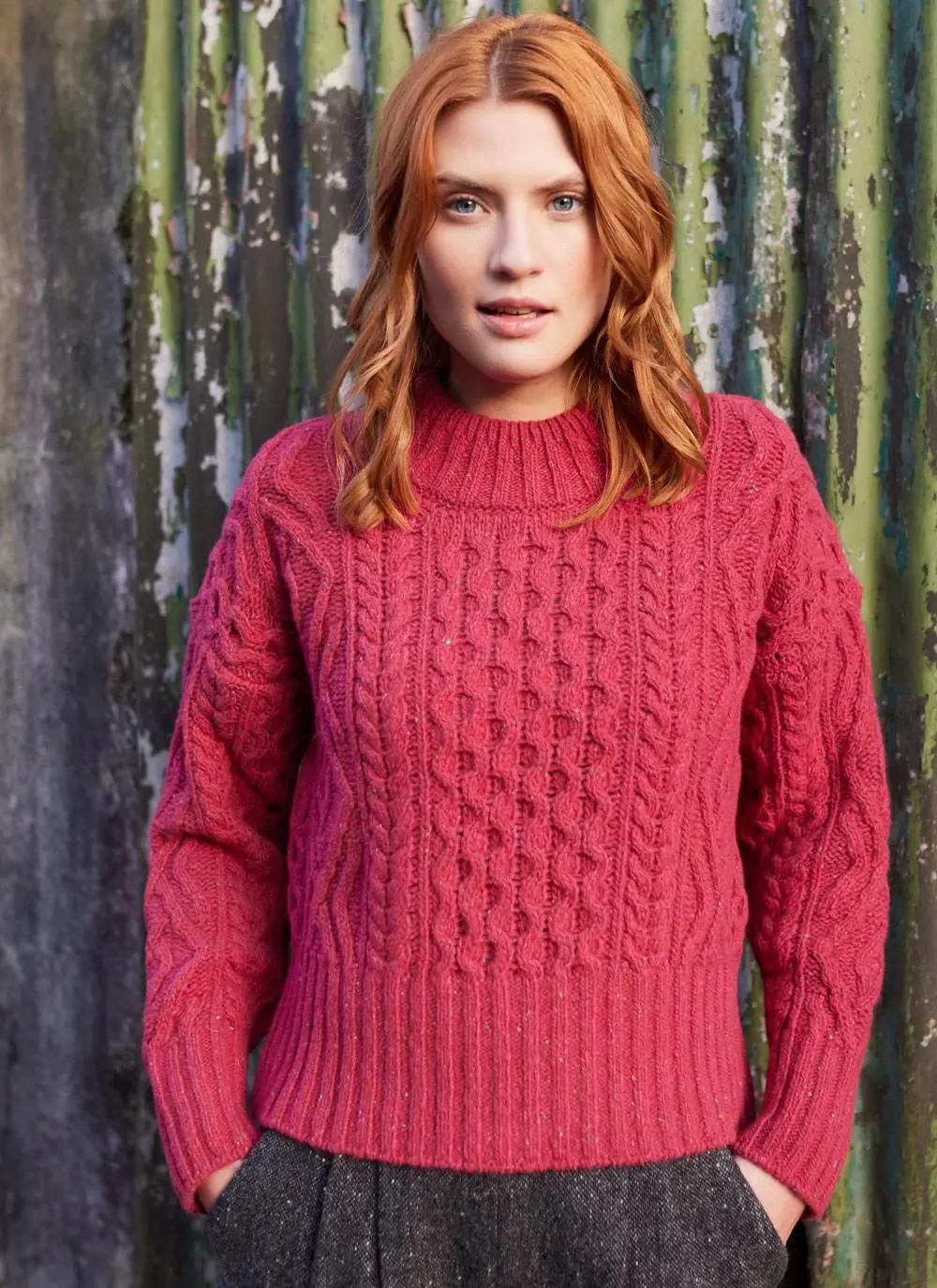 woman with red hair standing against fence wearing berry colored knit sweater