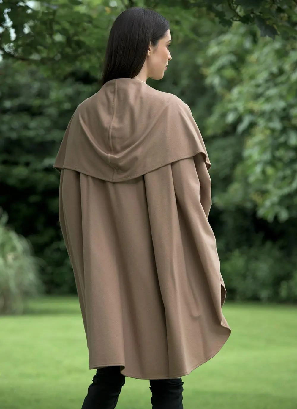 Back angle shot of brunette woman standing outside wearing camel cape.